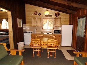 A cozy cabin-style kitchen with wooden cabinets, a dining table with chairs, a refrigerator, and a microwave. - Adorable Cabin with Indoor Jacuzzi in Arizona (Flagstaff)