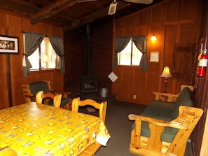 A cozy room with a wooden interior, a table with a yellow tablecloth, two chairs, a fireplace, and a lamp. - Adorable Cabin with Indoor Jacuzzi in Arizona (Flagstaff)