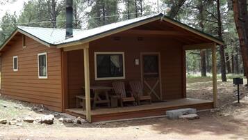 Une petite cabane en bois avec une véranda, deux chaises et une table.
