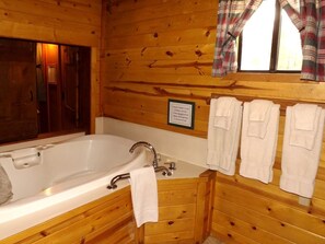 Une salle de bain rustique, aménagée dans une cabane en bois, avec une baignoire, un lavabo et un porte-serviettes avec des serviettes.