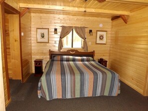 Une chambre dans une cabane en bois, avec un lit, deux tables de chevet et des tableaux encadrés accrochés aux murs.