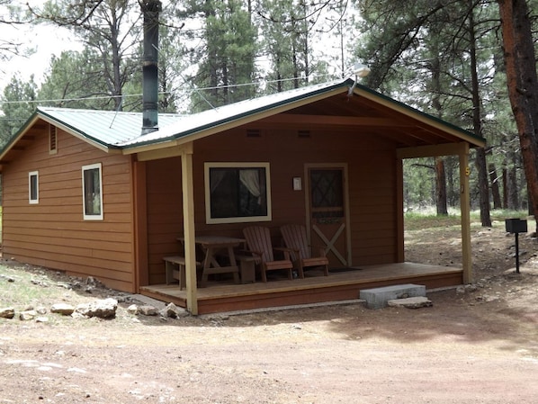 A small wooden cabin with a porch, two chairs, and a table. - Adorable Cabin with Indoor Jacuzzi in Arizona (Flagstaff)