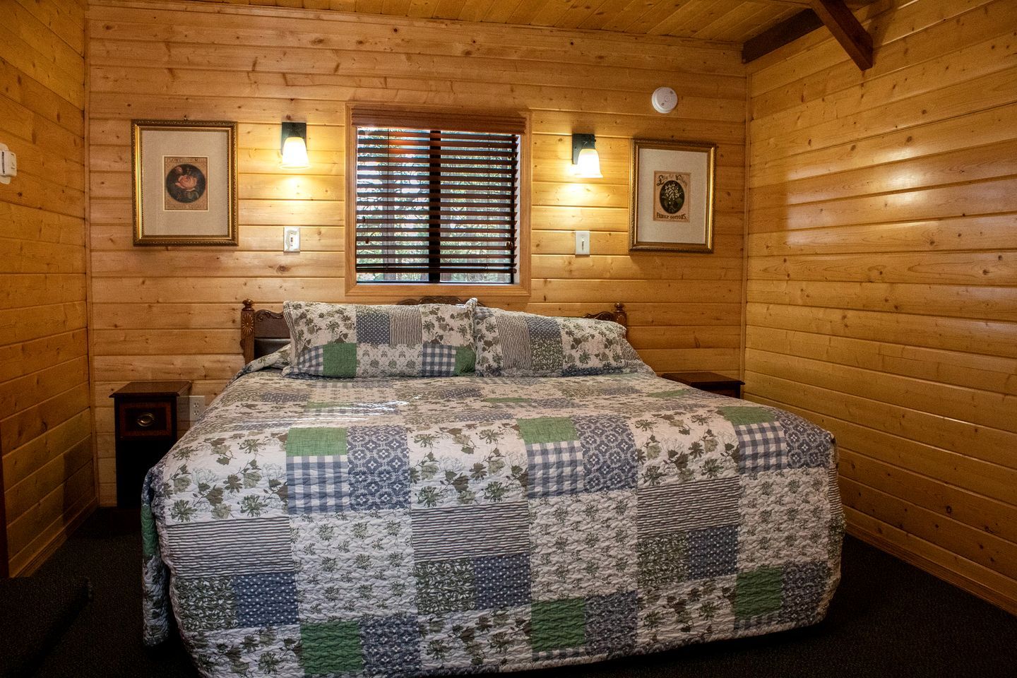 Habitación con paneles de madera, una cama, dos lámparas fijadas a la pared y cuadros enmarcados.