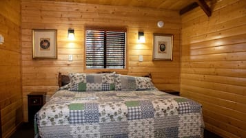 Habitación con paneles de madera, una cama, dos lámparas fijadas a la pared y cuadros enmarcados.