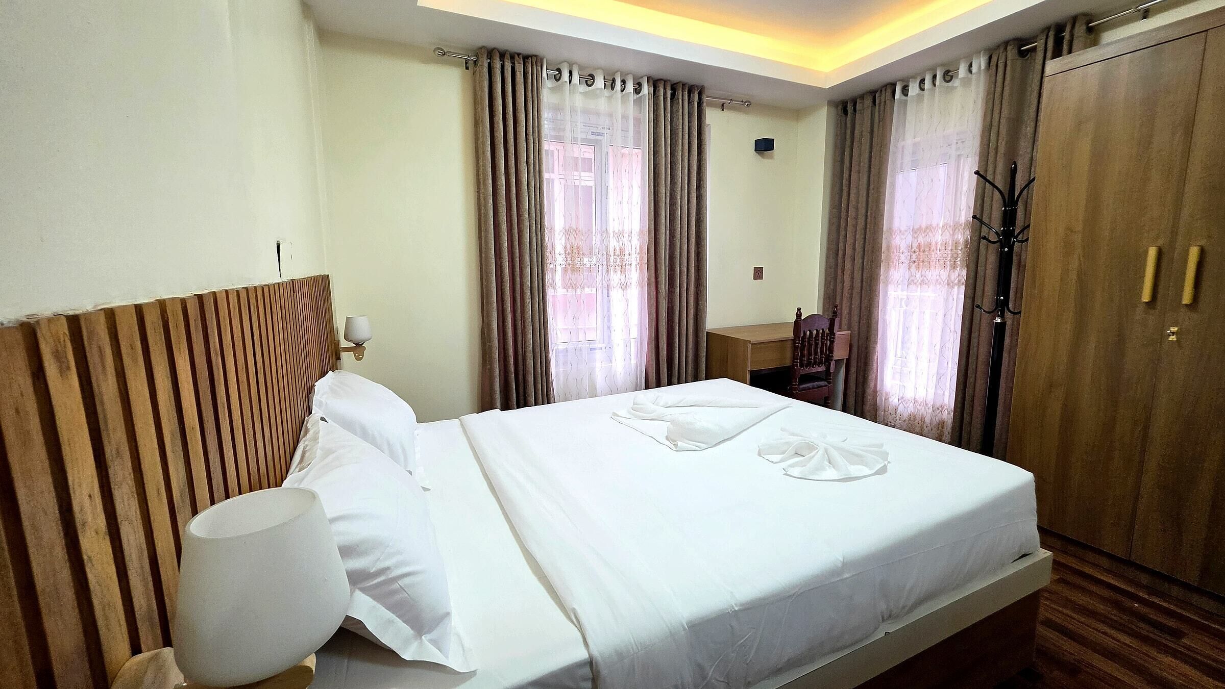 A hotel room with a bed, a wooden headboard, a desk, and a wardrobe.