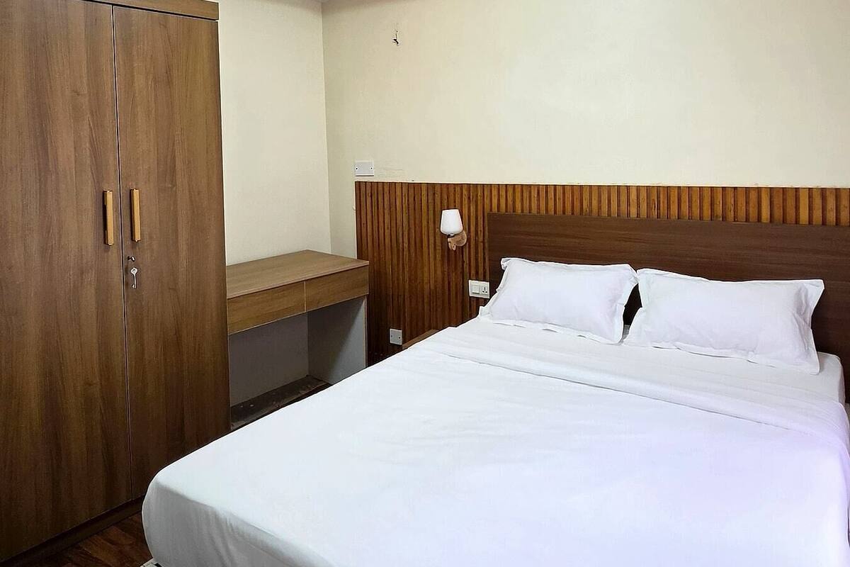 Una habitación de hotel con cama, armario de madera, mesita de noche, lámpara y luz de techo.