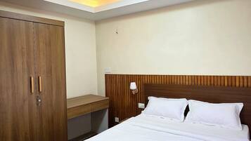 A hotel room with a bed, wooden wardrobe, bedside table, lamp, and a ceiling light.