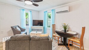 Un salon comprenant un canapé, un téléviseur, un ventilateur de plafond, une table à manger avec des chaises et une plante en pot.