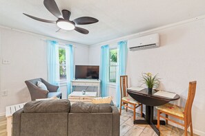 En stue med sofa, fjernsyn, loftventilator, spisebord med stole og en potteplante.