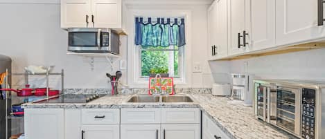 A modern kitchen with white cabinets, a stainless steel microwave, a built-in oven, and a coffee maker.