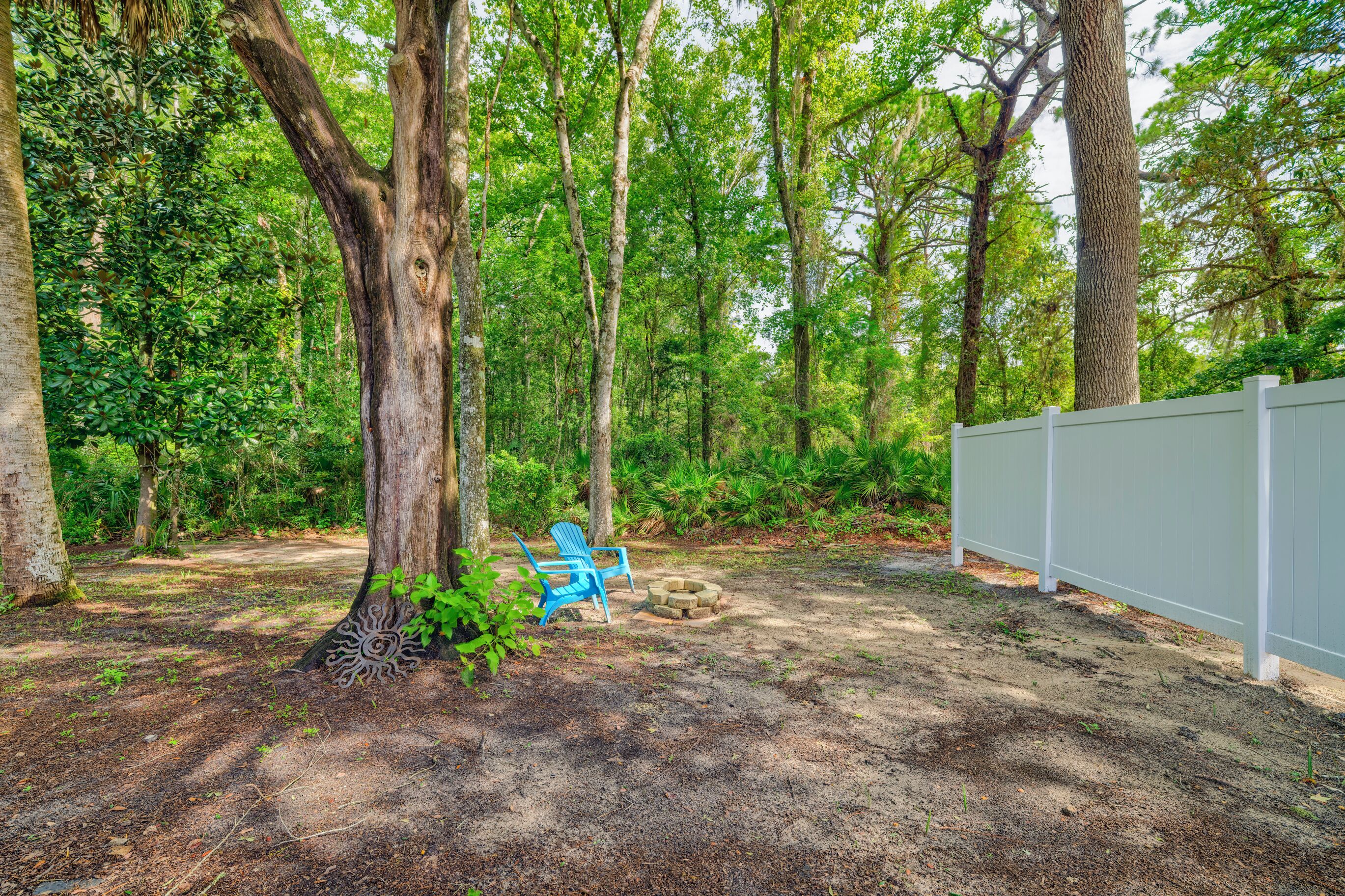 A forested area with a white fence, a blue chair, and a fire pit.