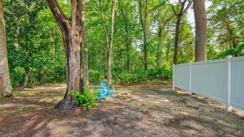 A forested area with a white fence, a blue chair, and a fire pit.