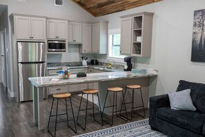 A modern kitchen with white cabinets, stainless steel appliances, a marble countertop, and a bar stool area. - Wooden Cabin Perfect for a Little Getaway in Livingston, Texas (Livingston)
