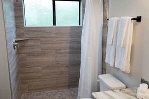 Ein Badezimmer mit einer Steinwand, einem Fenster, einem Duschvorhang, einer Toilette und Handtüchern an einem Ablagefach.