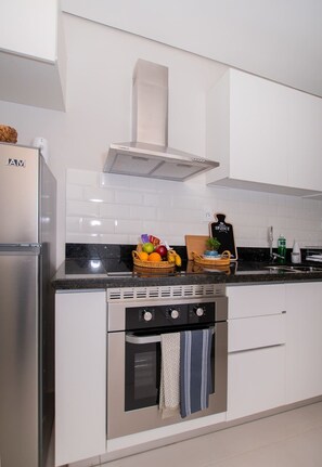 A modern kitchen with white cabinets, a stainless steel refrigerator, a built-in oven, and a range hood. - Corporate Stays First Living (Asunción)