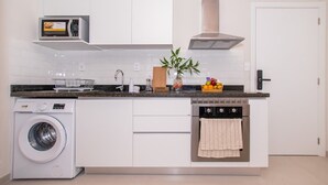 Cocina compacta con lavadora, microondas, horno y una pequeña isla con una planta.