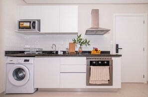 A compact kitchen with a washing machine, microwave, oven, and a small island with a plant. - Corporate Stays First Living (Asunción)