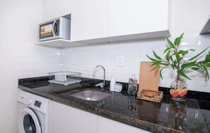 Una cocina con lavadora, microondas, fregadero y una planta.