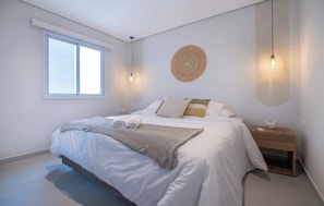 A bedroom with a bed, a bedside table, a wall-mounted light fixture, and a window. - Corporate Stays First Living (Asunción)