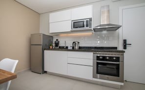A compact kitchen with white cabinets, a stainless steel refrigerator, a microwave, a gas stove, and a built-in oven. - Corporate Stays First Living (Asunción)