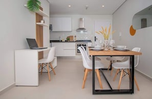 A modern kitchen with white cabinets, a stove, and a dining area with a table and chairs. - Corporate Stays First Living (Asunción)