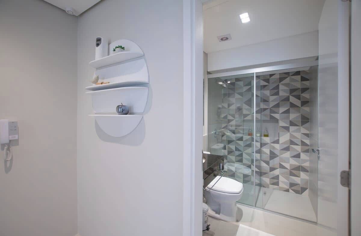 Un baño moderno con cabina de ducha de vidrio, inodoro y estante de pared.