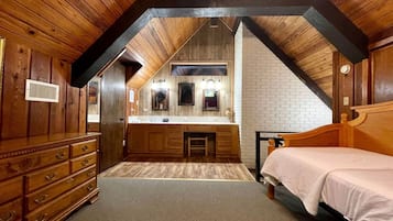 A bedroom with a wooden ceiling, a bed, a dresser, a vanity with a mirror, and a small stool.