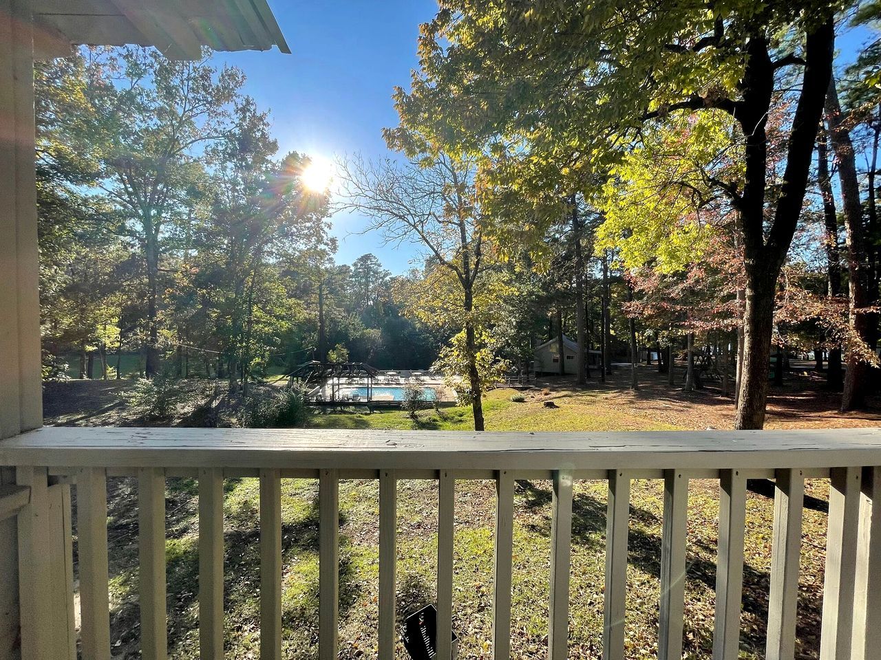 A wooden deck with a view of a swimming pool and trees.