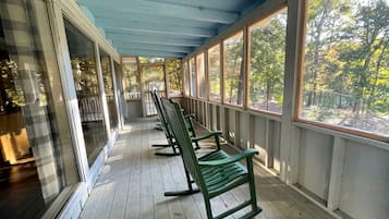 Une véranda couverte avec un plancher en bois et des fauteuils à bascule verts.