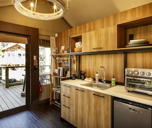 A modern kitchen with wooden cabinetry, a stainless steel sink, a built-in oven, and a wooden deck outside.