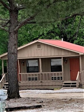 A single-story cabin with a porch, a red door, and a chimney.