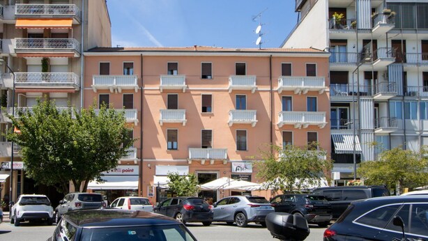 Un edificio de varios pisos con balcones, un estacionamiento y cielo despejado.