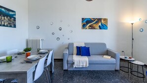 Una sala de estar moderna con comedor, un sofá gris con cojines azules, una mesa de centro y un cuadro en la pared.