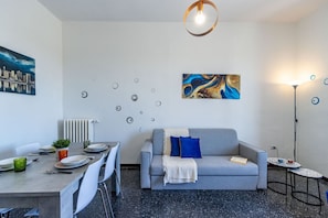Ein modernes Wohnzimmer mit Essbereich, ein graues Sofa mit blauen Kissen, einem Couchtisch und einem Bild an der Wand.