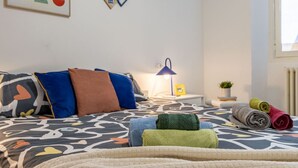 Una cama bien hecha con ropa de cama estampada, una lámpara de noche y una pequeña planta en maceta sobre una mesita de noche.