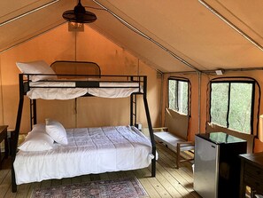 A tented room with bunk beds, a small desk, and a refrigerator.