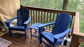 A wooden deck with two blue Adirondack chairs and a small table.