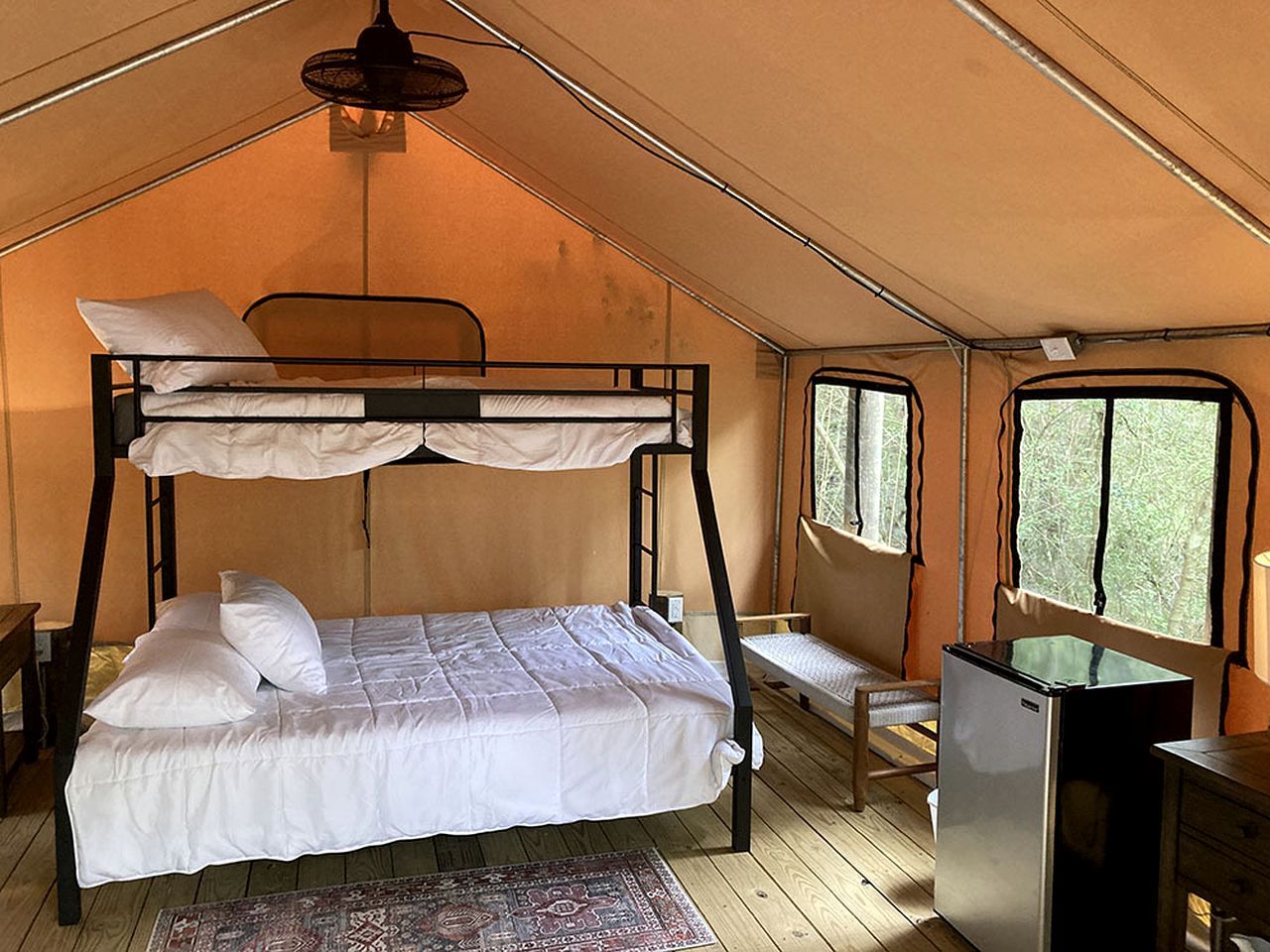 A tented room with bunk beds, a small desk, and a refrigerator.