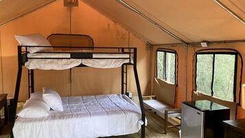 A tented room with bunk beds, a small desk, and a refrigerator.