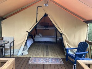 A tented accommodation with a bunk bed, a small table, and a chair.