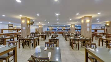 A spacious dining area with multiple wooden tables and chairs, a central counter, and ceiling lights.