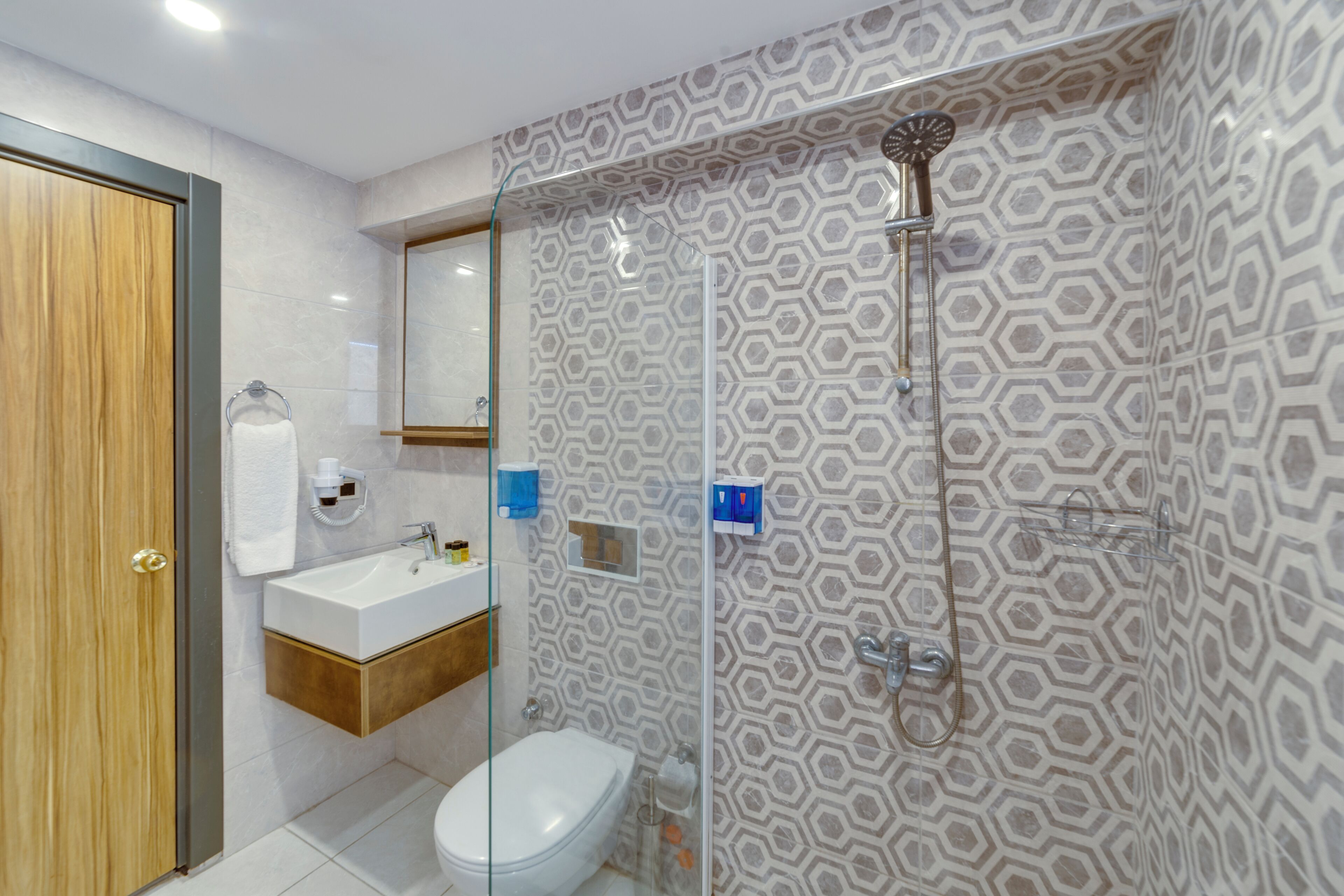 Un baño moderno con cabina de ducha de vidrio, puerta de madera y lavabo blanco.