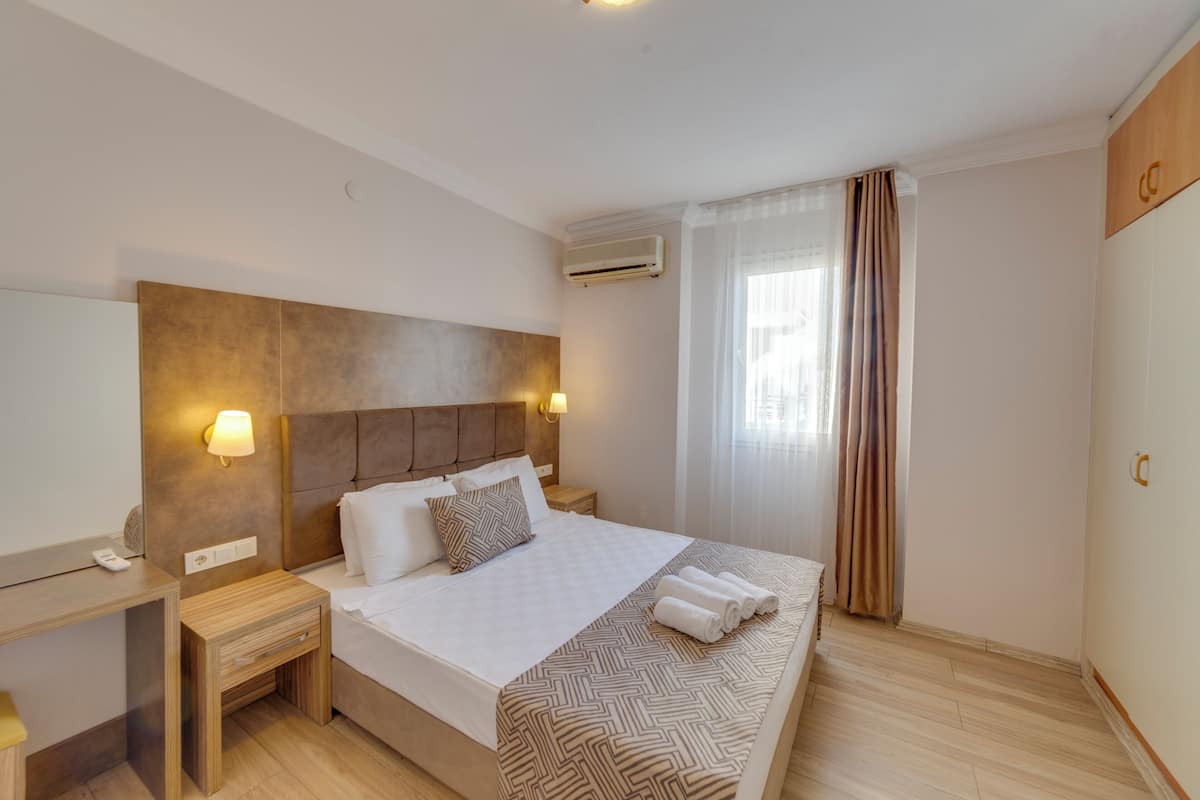 Une chambre d’hôtel avec un grand lit, des tables de chevet, un appareil de climatisation et une fenêtre avec des rideaux.