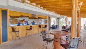 Una terraza de madera con zona de bar, taburetes y una mesa redonda de madera.