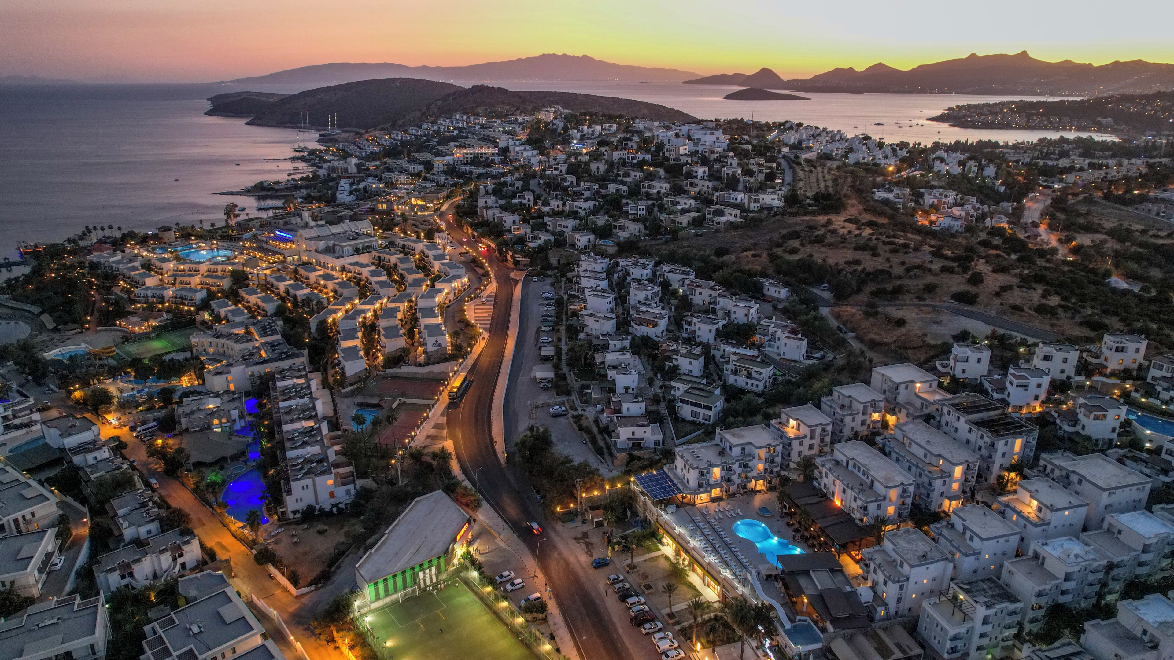 An aerial view of a coastal town with white buildings, a main road, and a body of water.
