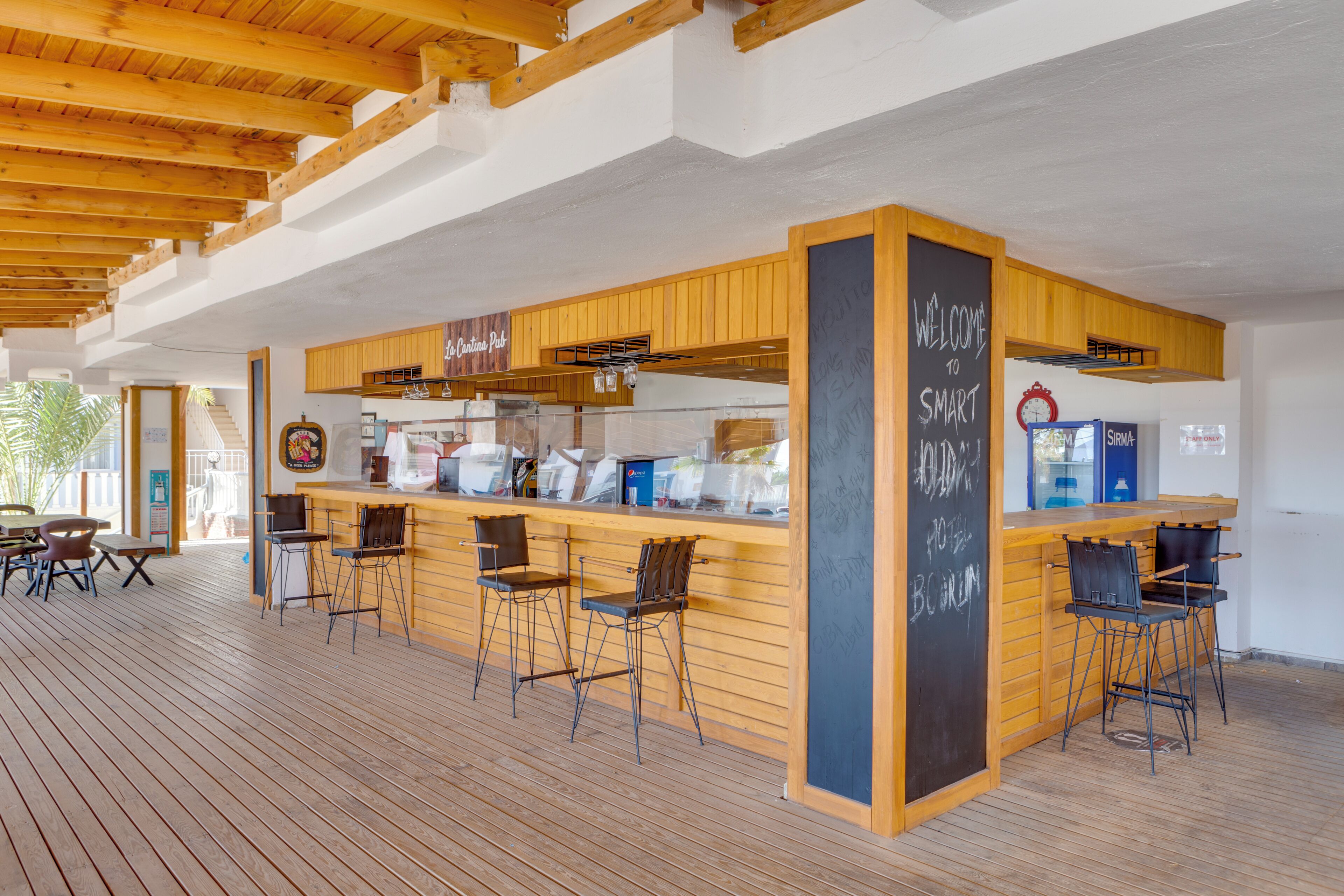 A wooden bar area with bar stools, a chalkboard with 'WELCOME TO SMART' written on it, and a sign for 'The Coastal Pub'.