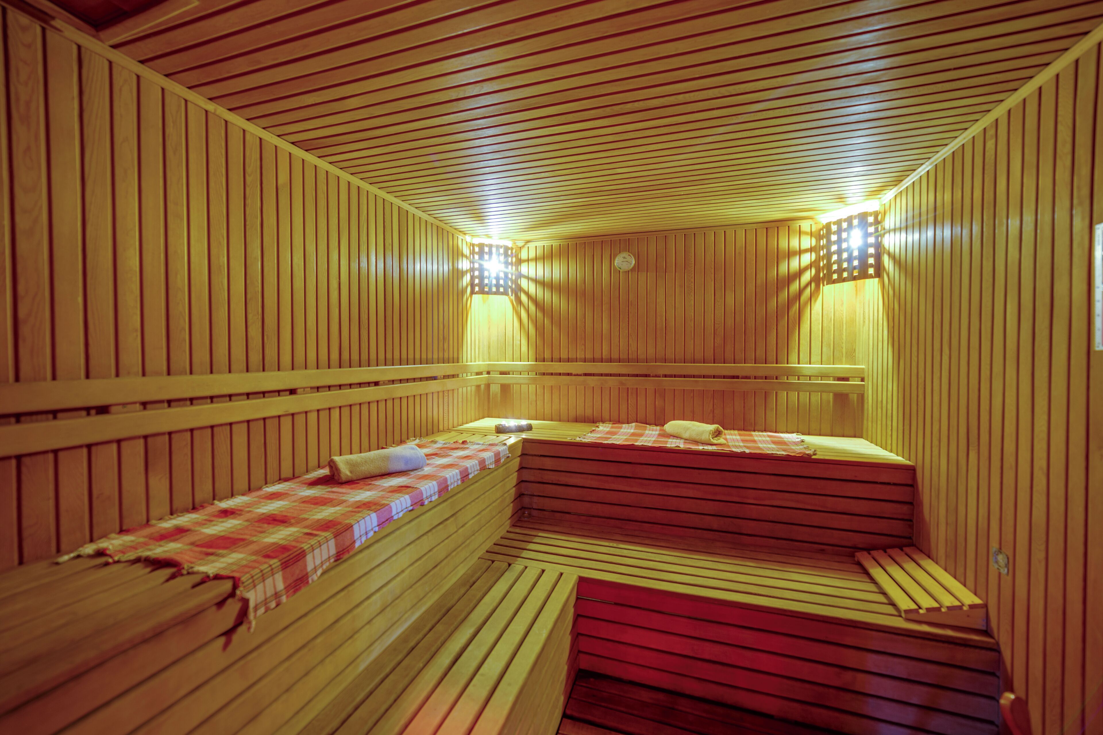 A sauna room with wooden benches and benches, a checkered towel, and a wall-mounted light fixture.