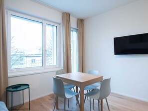 Ein modernes Zimmer mit einem Holztisch, vier Stühlen, einem an der Wand befestigten Fernseher und einem Fenster mit Vorhängen.