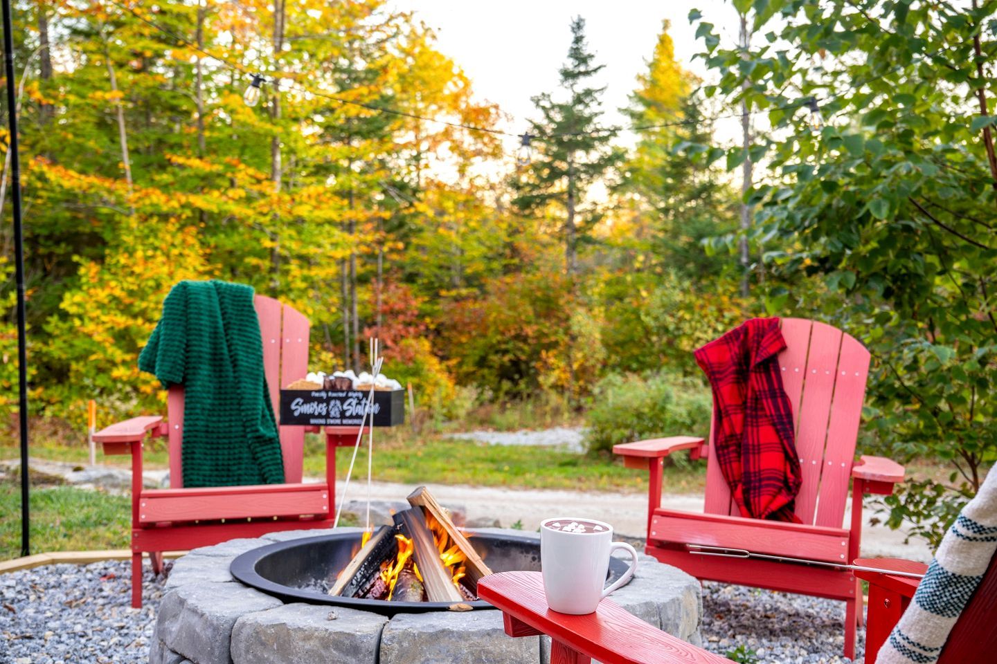 Un foyer avec deux chaises Adirondack rouges, un panneau et une tasse.