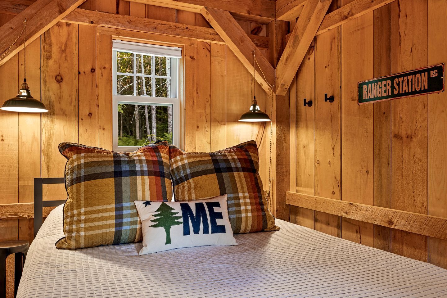 A cozy cabin room with a bed, plaid pillows, a window, and a sign reading 'RANGER STATION.'